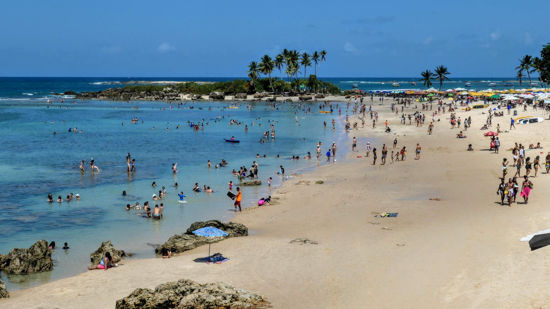 Strand in Morro de São Paulo, Brasilien, mit vielen Einheimischen im türkisblauen Wasser und unter Palmen.