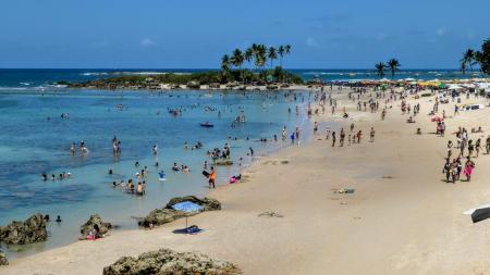 Strand in Morro de São Paulo, Brasilien, mit vielen Einheimischen im türkisblauen Wasser und unter Palmen.