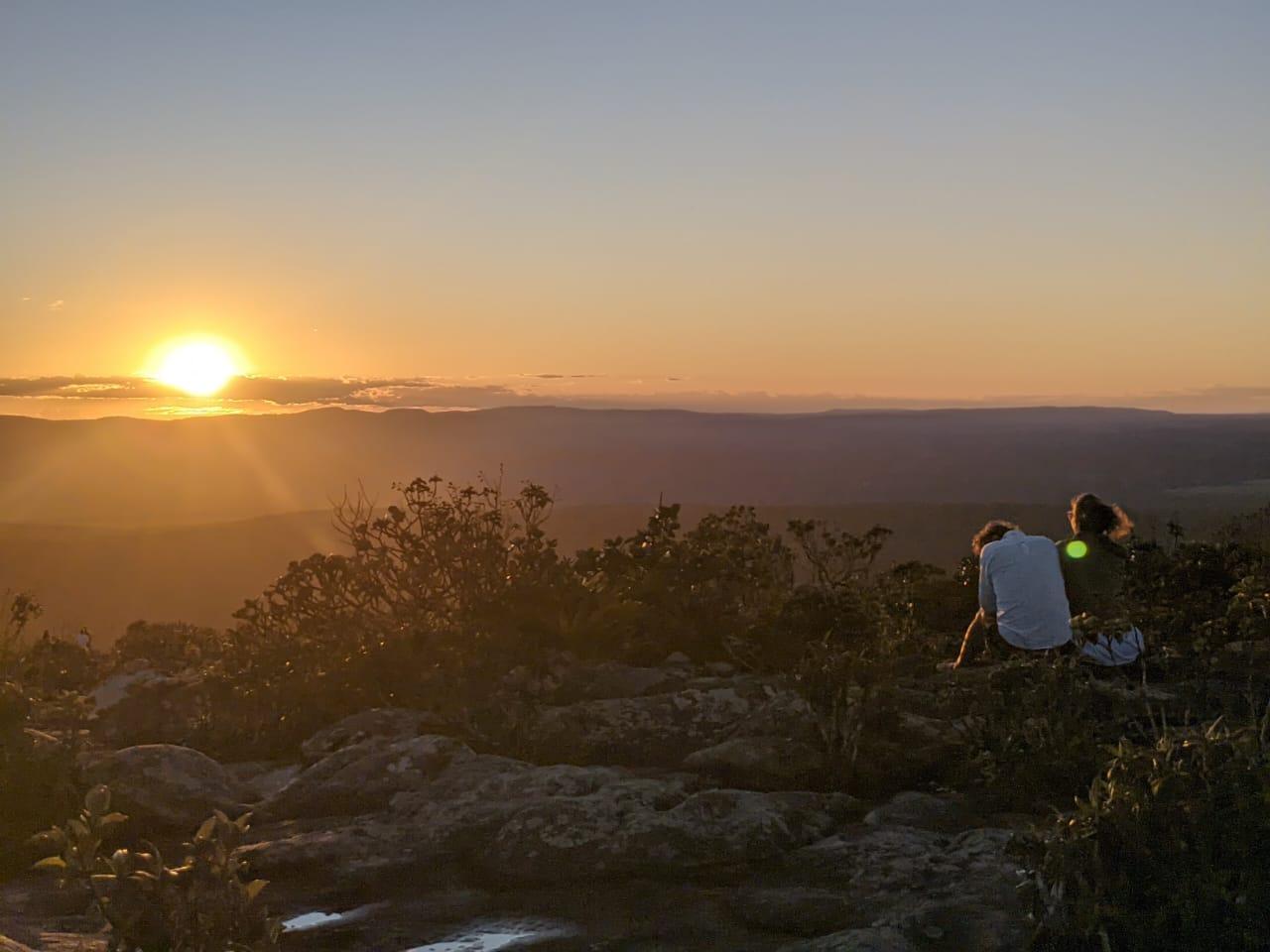 Zwei Personen sitzen auf dem Morro do Pai Inacio und schauen den Sonnenuntergang an